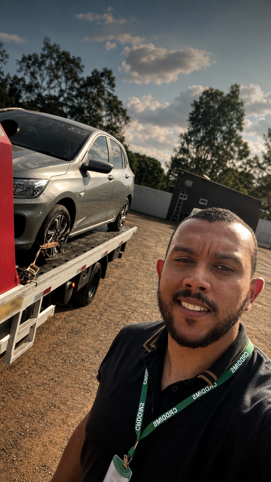 Selfie de Nilmar ao ar livre, ao lado de um carro em cima de um guincho